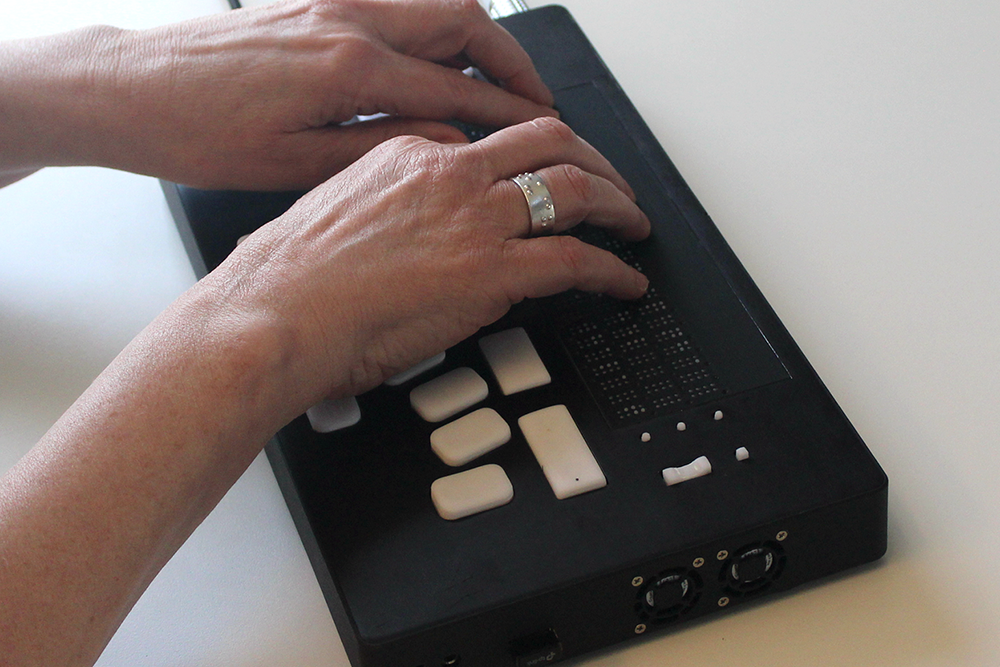 Person using a braille display device with their hands on a white surface