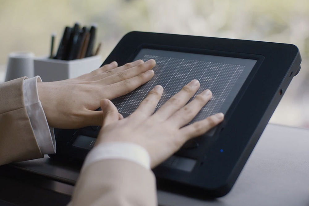 Person using a digital DotPad with a grid layout on a blurred background