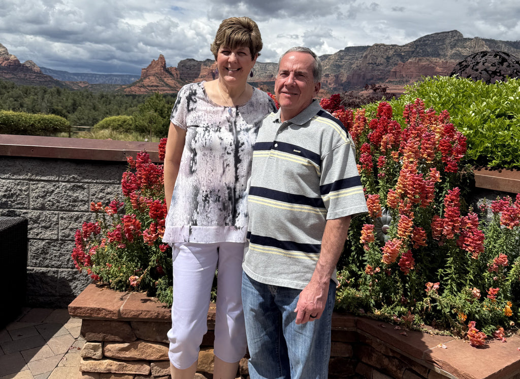 Kimberly and her husband standing in front of flowers and a scenic view of canyon formations